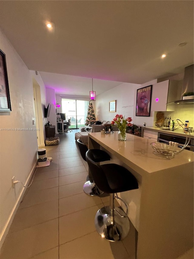 kitchen featuring a breakfast bar area, a kitchen island, light countertops, white cabinets, and wall chimney range hood