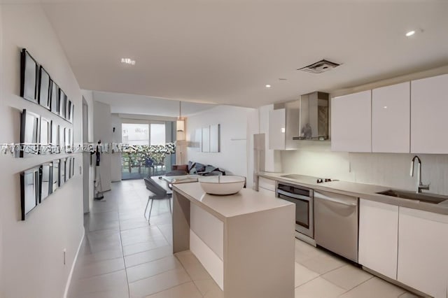 kitchen with wall chimney exhaust hood, stainless steel appliances, sink, white cabinetry, and a kitchen island