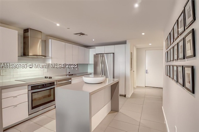 kitchen featuring white cabinetry, a center island, wall chimney exhaust hood, stainless steel appliances, and decorative backsplash