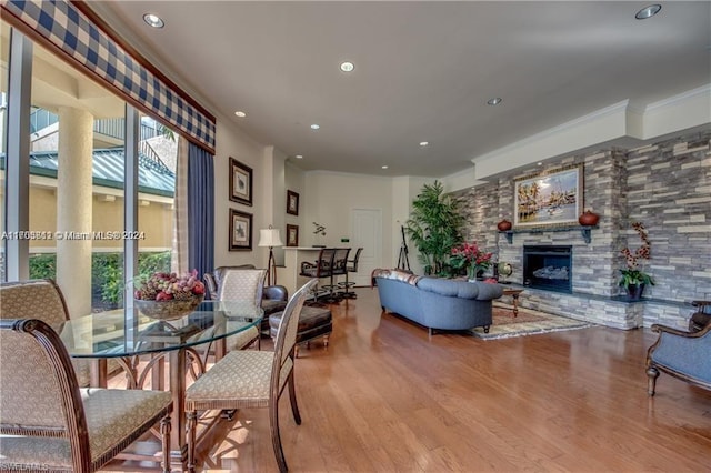 dining area with a stone fireplace, light hardwood / wood-style floors, and ornamental molding