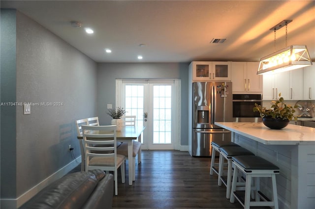 kitchen with appliances with stainless steel finishes, dark wood-type flooring, white cabinets, hanging light fixtures, and a breakfast bar area