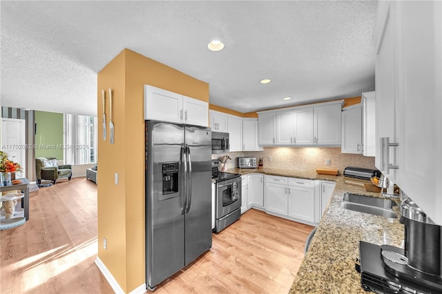 kitchen featuring light stone countertops, white cabinetry, light wood-type flooring, and appliances with stainless steel finishes