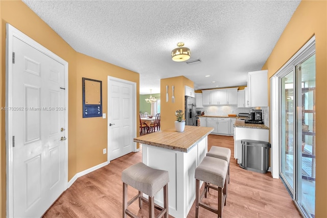 kitchen with stainless steel refrigerator with ice dispenser, a kitchen breakfast bar, a center island, light hardwood / wood-style floors, and white cabinetry