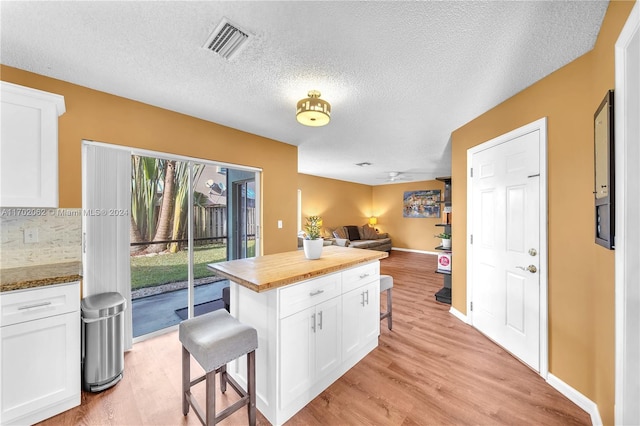 kitchen with a kitchen breakfast bar, white cabinetry, light hardwood / wood-style floors, and a textured ceiling