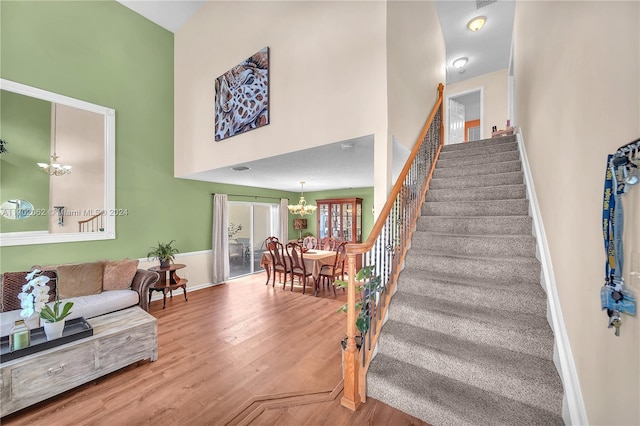 stairs featuring a chandelier, wood-type flooring, and a high ceiling