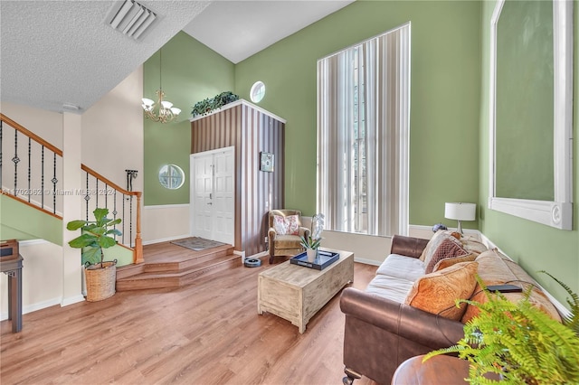 living room with a chandelier, a textured ceiling, high vaulted ceiling, and light hardwood / wood-style flooring