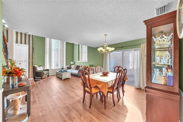 dining room with a wealth of natural light, an inviting chandelier, a textured ceiling, and light wood-type flooring