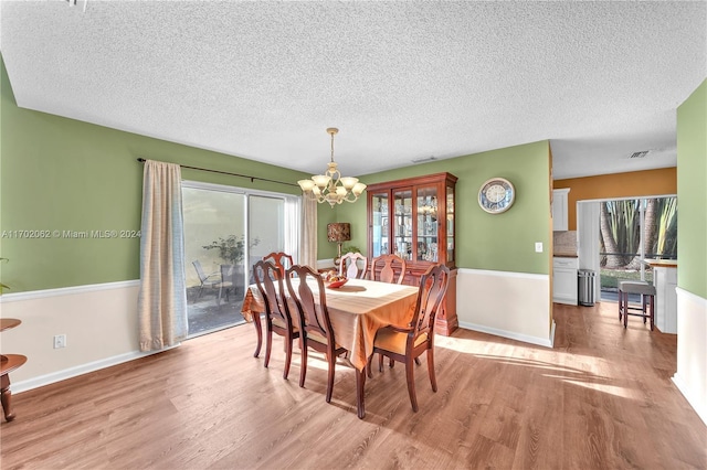 dining space featuring light wood-type flooring, a textured ceiling, and an inviting chandelier