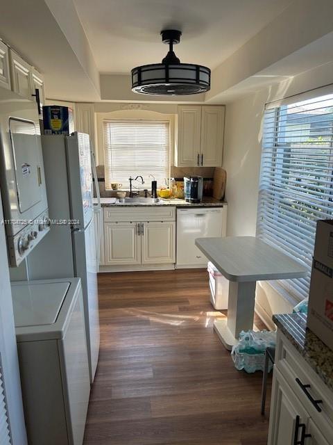 kitchen featuring white cabinetry, dishwasher, dark wood-type flooring, stacked washer / dryer, and decorative light fixtures