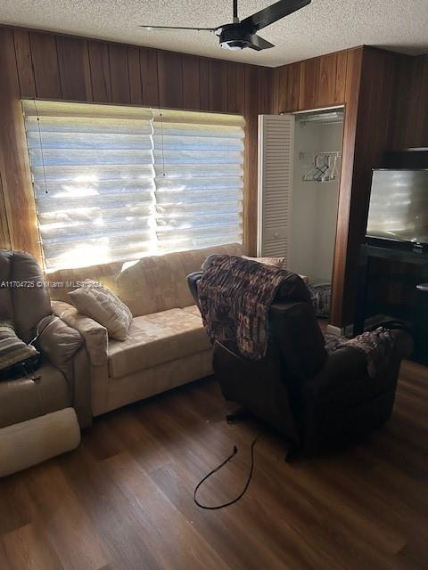 living room featuring ceiling fan, a textured ceiling, wooden walls, and dark wood-type flooring