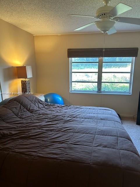 carpeted bedroom with ceiling fan, a textured ceiling, and multiple windows