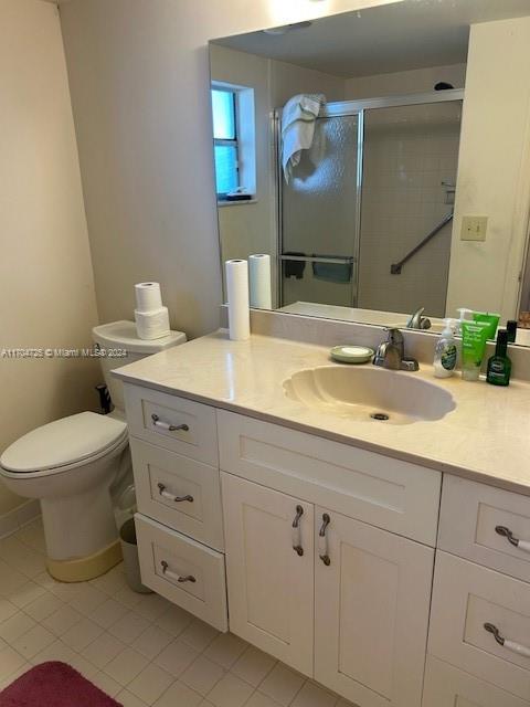 bathroom with tile patterned flooring, vanity, toilet, and a shower with shower door