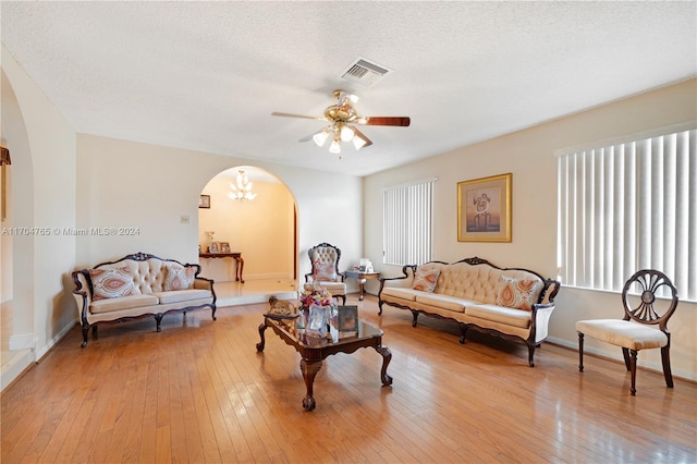 living room with ceiling fan with notable chandelier, a textured ceiling, and light wood-type flooring