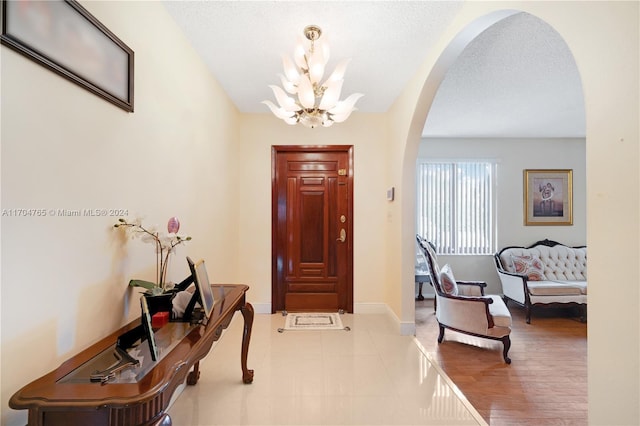 entryway with light hardwood / wood-style floors, a textured ceiling, and a notable chandelier