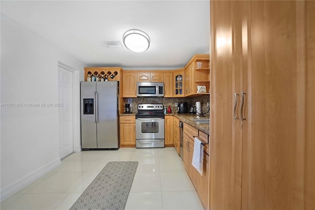 kitchen with backsplash, light tile patterned flooring, dark stone counters, and appliances with stainless steel finishes