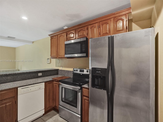 kitchen with appliances with stainless steel finishes, light tile patterned floors, and dark stone countertops