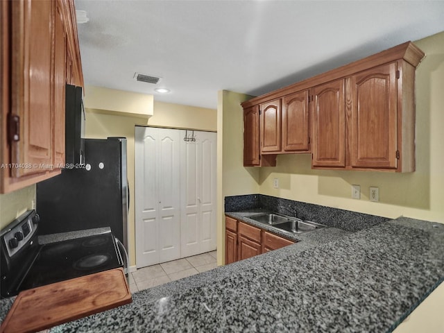 kitchen featuring dark stone countertops, sink, light tile patterned floors, and black appliances