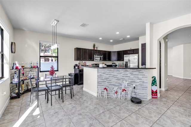 kitchen featuring dark brown cabinets, a healthy amount of sunlight, stainless steel appliances, and hanging light fixtures