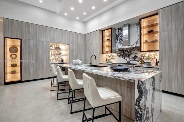 kitchen featuring a kitchen breakfast bar, light stone counters, a spacious island, sink, and wall chimney range hood