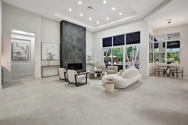 living room with ceiling fan, a fireplace, a high ceiling, and a tray ceiling