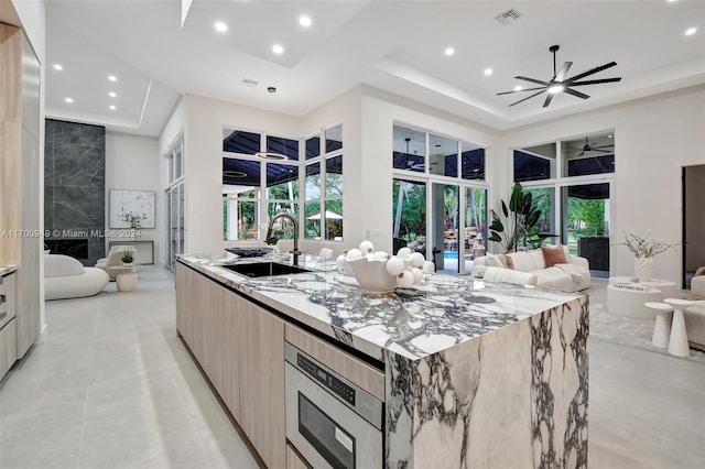 kitchen featuring sink, light stone counters, a towering ceiling, a spacious island, and a tray ceiling