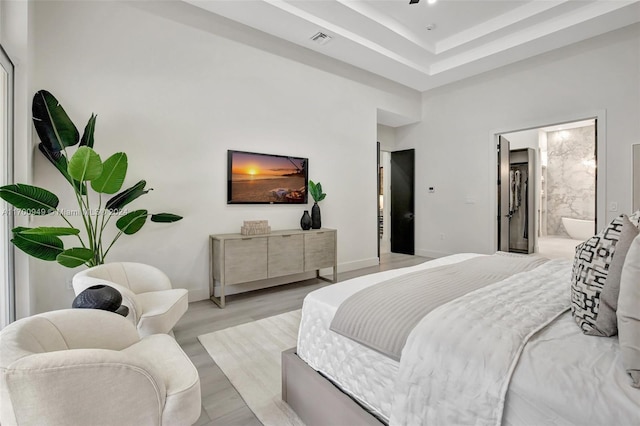 bedroom featuring a raised ceiling, connected bathroom, and light hardwood / wood-style floors