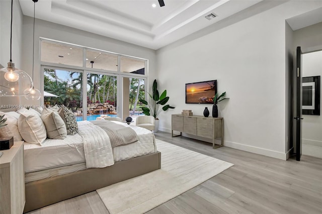 bedroom with ceiling fan, a raised ceiling, and light hardwood / wood-style flooring