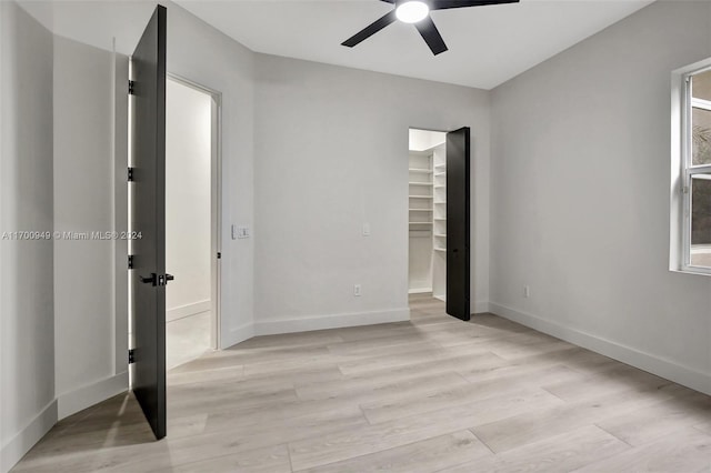 unfurnished bedroom featuring a closet, light hardwood / wood-style flooring, a spacious closet, and ceiling fan