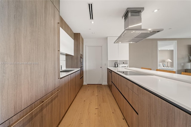 kitchen featuring black electric stovetop, light countertops, island range hood, and modern cabinets