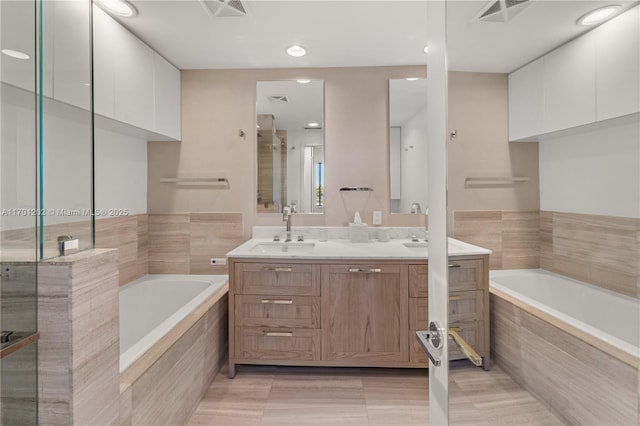 bathroom with visible vents, double vanity, a sink, and a bath