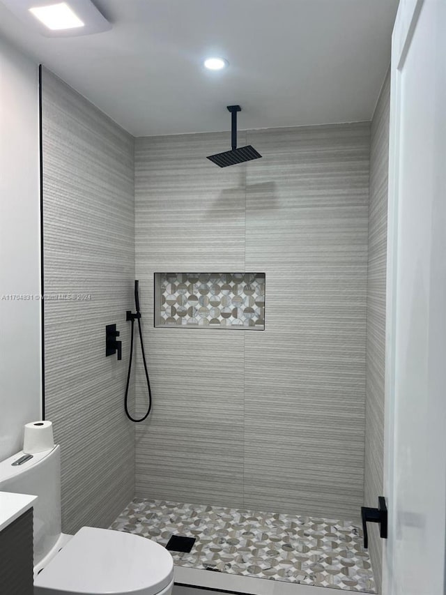 bathroom with a tile shower, vanity, and toilet