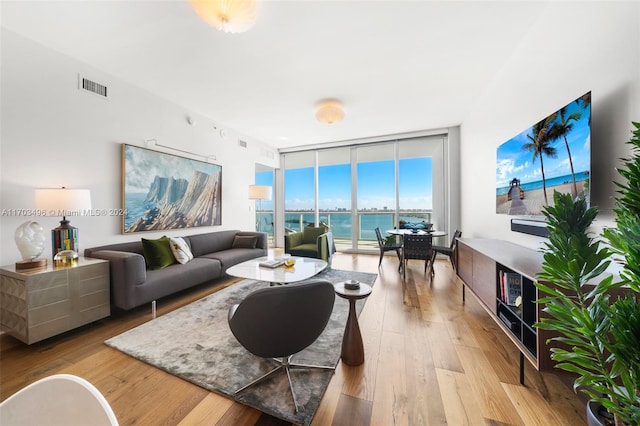 living room with expansive windows, a water view, and light hardwood / wood-style floors