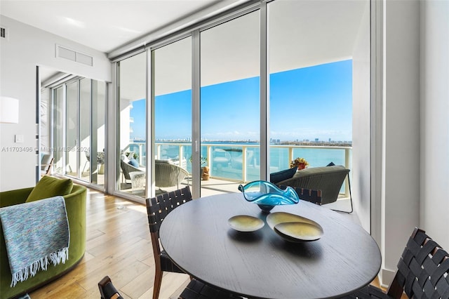 dining area featuring expansive windows, a wealth of natural light, a water view, and light hardwood / wood-style floors