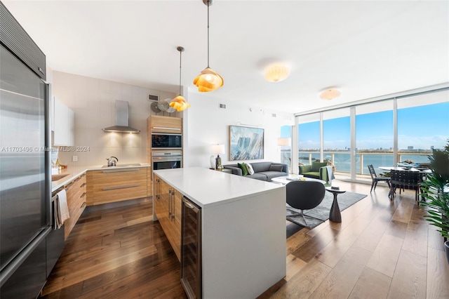 kitchen featuring hanging light fixtures, wall chimney range hood, tasteful backsplash, built in appliances, and a water view