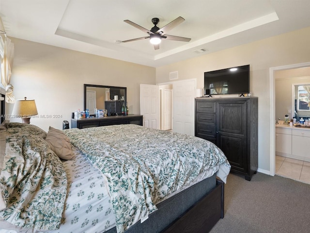 carpeted bedroom with ensuite bathroom, a raised ceiling, and ceiling fan