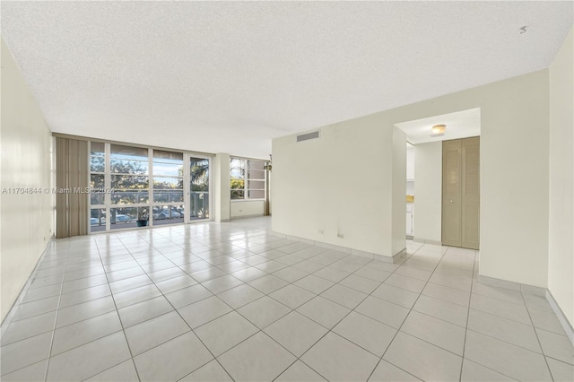 tiled empty room featuring a textured ceiling and floor to ceiling windows