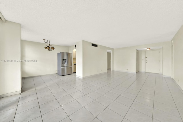 empty room with a chandelier, light tile patterned floors, and a textured ceiling