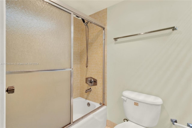 bathroom featuring toilet and shower / bath combination with glass door