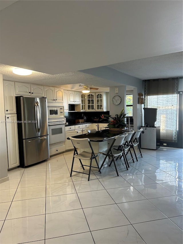 kitchen with a textured ceiling, white cabinets, light tile patterned floors, and white appliances