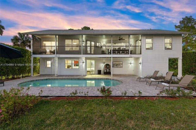 back house at dusk featuring a patio, a balcony, ceiling fan, and a lawn