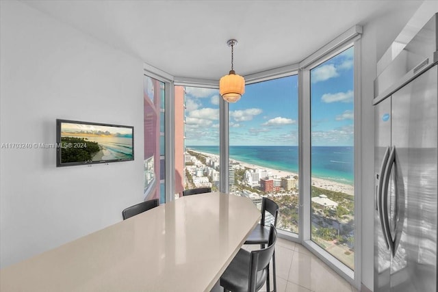 dining space with light tile patterned floors, a water view, a view of the beach, and a wall of windows