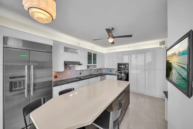 kitchen featuring a kitchen bar, tasteful backsplash, a spacious island, black appliances, and white cabinets