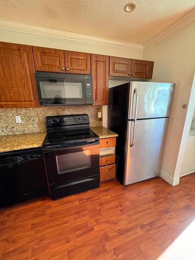 kitchen featuring light stone countertops, backsplash, crown molding, black appliances, and wood-type flooring