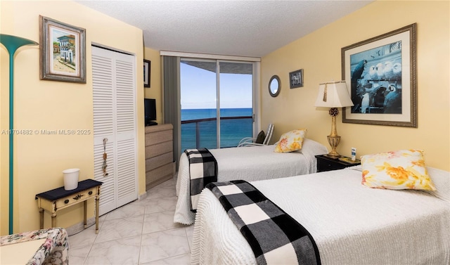 bedroom featuring access to exterior, a textured ceiling, a wall of windows, and a closet