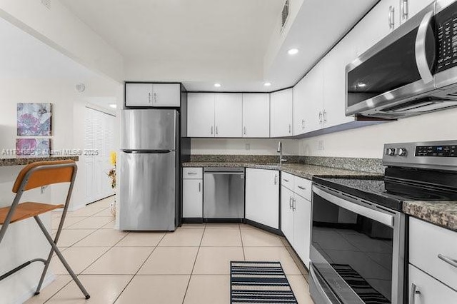 kitchen featuring light tile patterned floors, recessed lighting, a sink, white cabinets, and appliances with stainless steel finishes