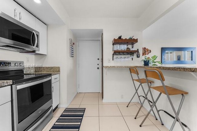 kitchen with a breakfast bar area, open shelves, stainless steel appliances, light tile patterned floors, and white cabinetry