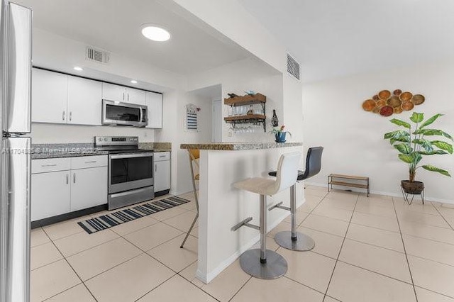 kitchen featuring a breakfast bar area, light tile patterned floors, stainless steel appliances, visible vents, and a peninsula