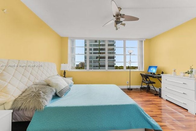 bedroom with a ceiling fan, multiple windows, baseboards, and wood finished floors