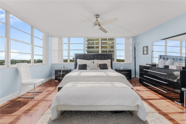 bedroom featuring baseboards, a ceiling fan, wood finished floors, and multiple windows