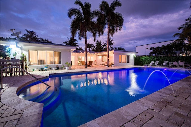 pool at dusk featuring pool water feature and a patio